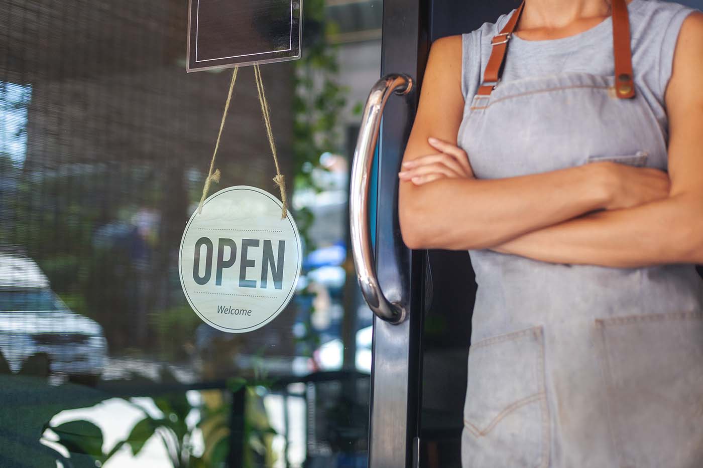 Small business owner standing in front of her shop. It is important to improve your local SEO to attract more customers