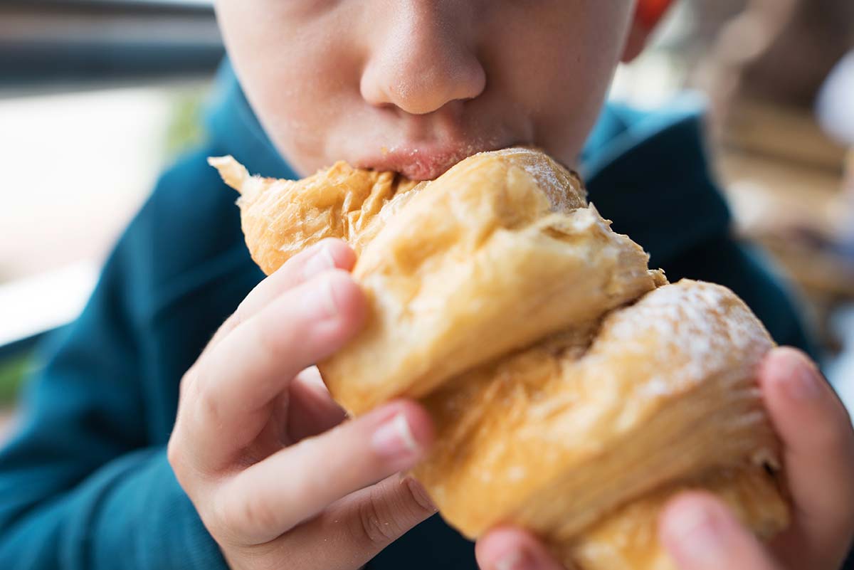 A boy taking a bite out of a delicious croissant at a bakery as an example of how Psychology Can Revolutionize Your Small Business Marketing