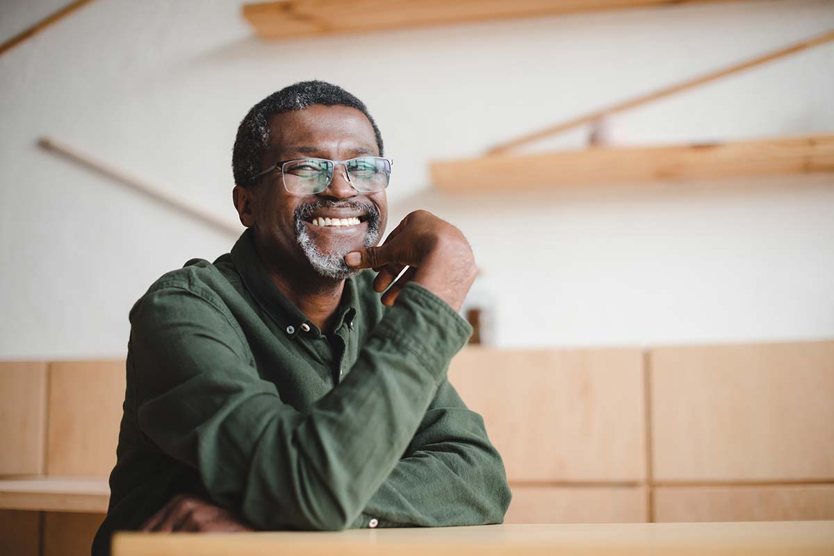 Smiling man with glasses sitting at a wooden desk, radiating confidence and warmth.