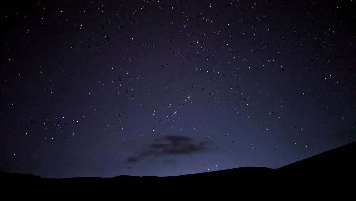 Star-filled night sky over a dark mountain landscape