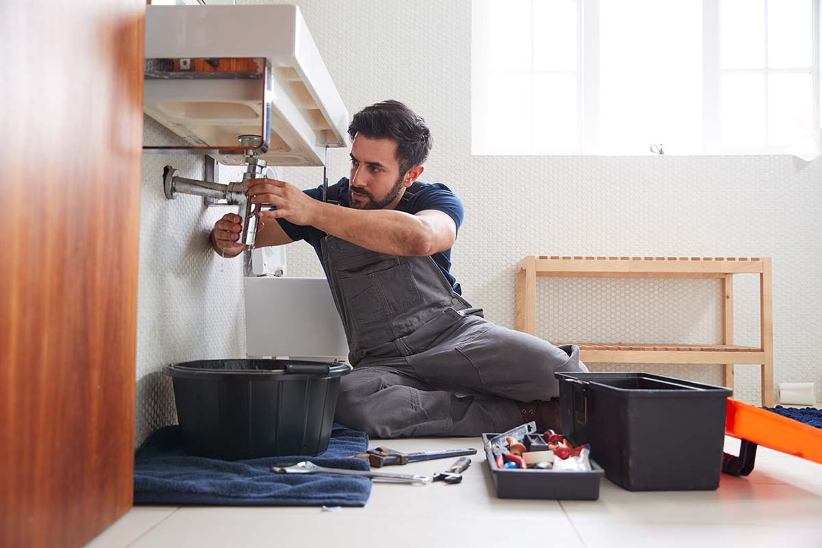Alt tag: Plumber repairing pipes beneath a bathroom sink